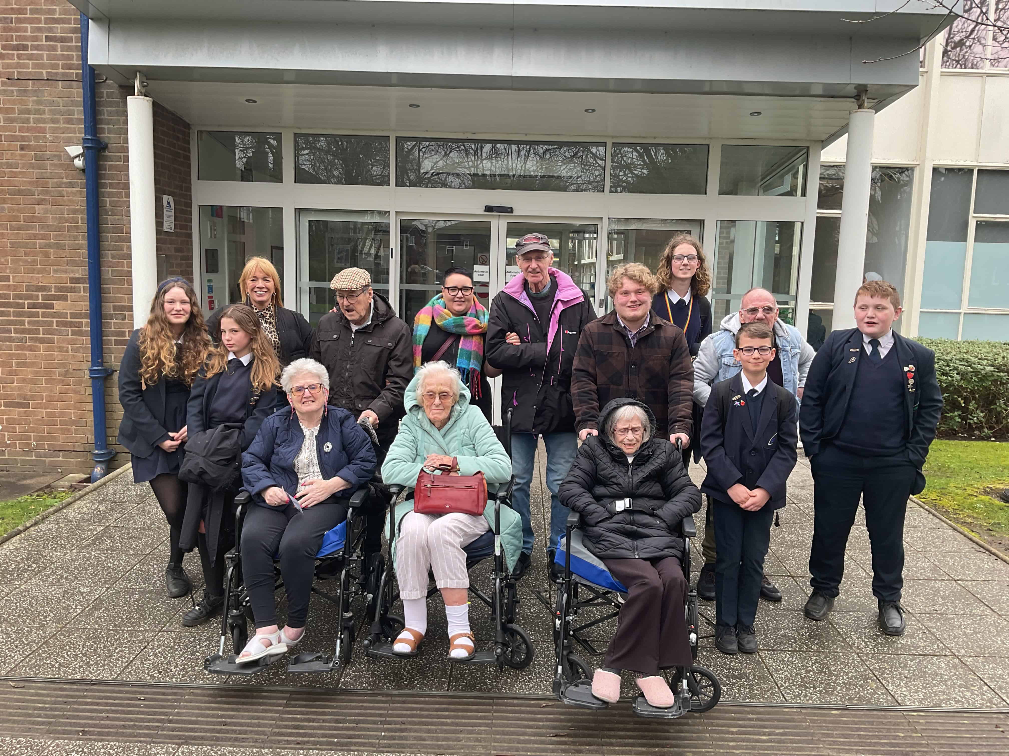 Students from the Priestnall School Council smile alongside residents of Priestnall Court outside the school entrance.