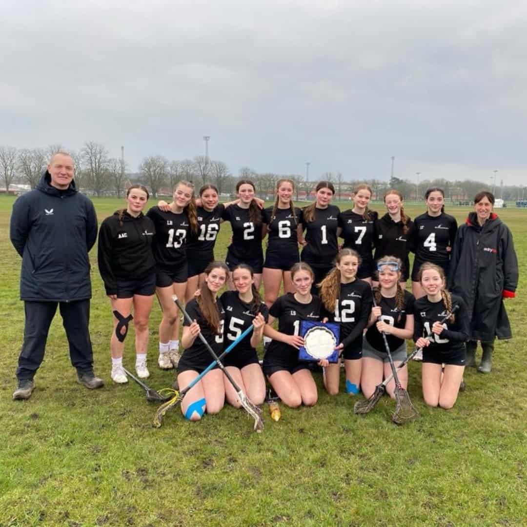 Priestnall School Under 15s Girls Lacrosse Team smile on the field with their coach.