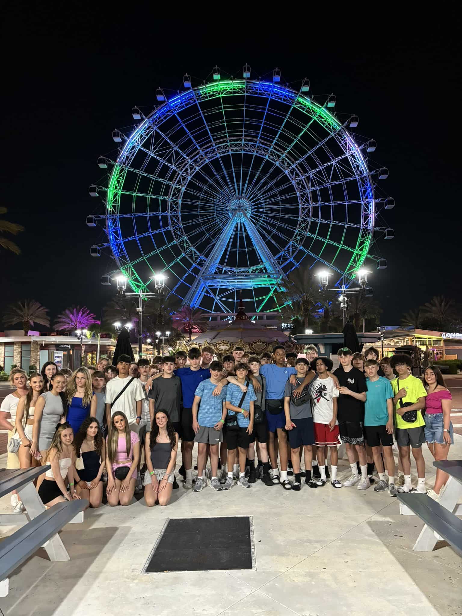 Priestnall School students stand in a large group in front of a ferris wheel in the USA on a trip.