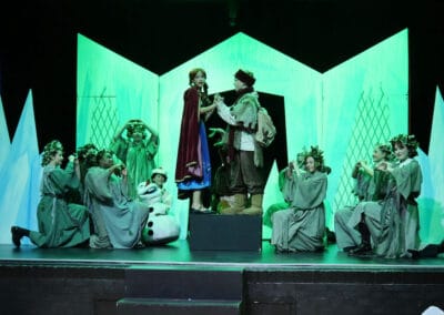 Two Priestnall School students hold hands and sing a duet surrounded by students kneeling on stage in the Priestnall School Frozen Jr Production.