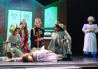 Students kneel on the ground in a circle around a student lying on the floor while performing in the Priestnall School Frozen Jr Production.