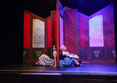 Two students, acting as Anna and Elsa, sit in separate rooms with their backs against either side of the connecting wall in the Priestnall School Frozen Jr Production.