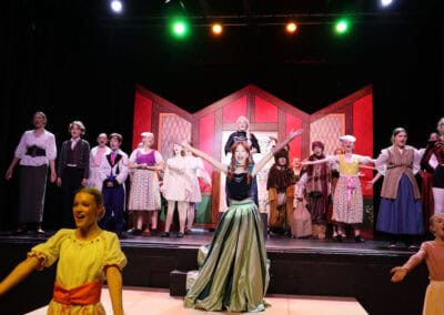 A student acting as Anna stands with her arms in the air during an ensemble song in the Priestnall School Frozen Jr Production.