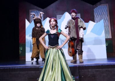 A student acting as Anna stands with her hands on her hips, a reindeer and Kristoff stand behind her in the Priestnall School Frozen Jr Production.