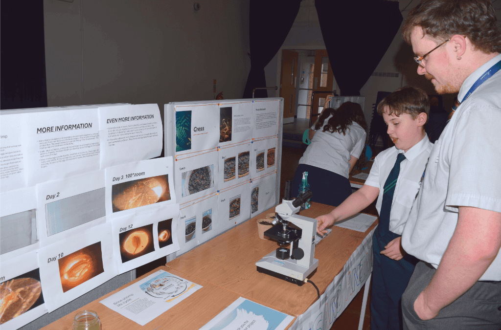 A student from Priestnall School explains his research project to a teacher at the Science Fair 2024.